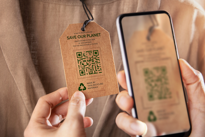 På bilden syns att någon håller upp en mobiltelefon för att scanna en qr-kod på en etikett som sitter på ett klädesplagg.