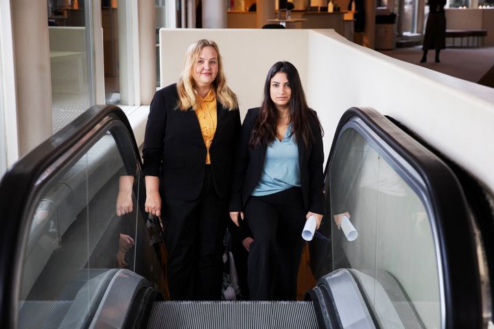 Ida Gabrielsson och Nooshi Dadgostar åker upp i rulltrappan i Riksdagen och tittar in i kameran.
