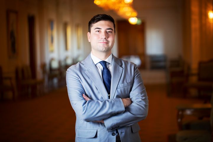 Andreas Lennkvist Manriquez från Vänsterpartiet står i en blå kavaj med korsade armar och tittar in i kameran.