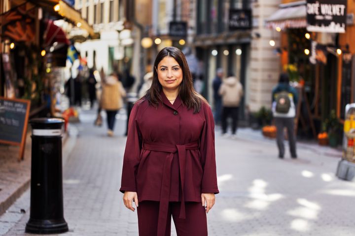 Nooshi står på en gata i stan med människor omkring sig och tittar in i kameran.