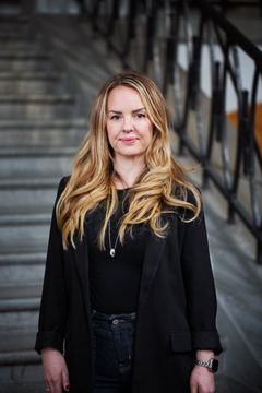 Hannah Dahlbäck står i trappen i Landstingshuset i Stockholm och tittar in i kameran. Hon har en svart tröja på sig.