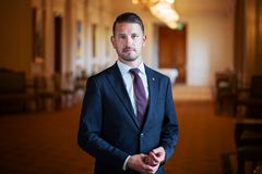 Samuel står och tittar in i kameran. Han har en blå kavaj och slips på sig. Han står i en riksdagskorridor.