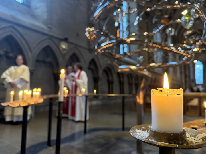 Ljus i ljusträd i förgrunden med präst- och diakonkandidater i bakgrunden.