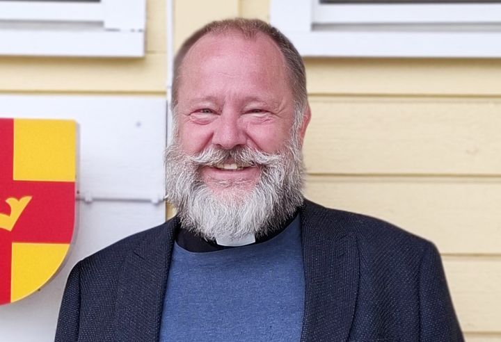 Kyrkoherde Magnus Svensson framför gul husvägg.