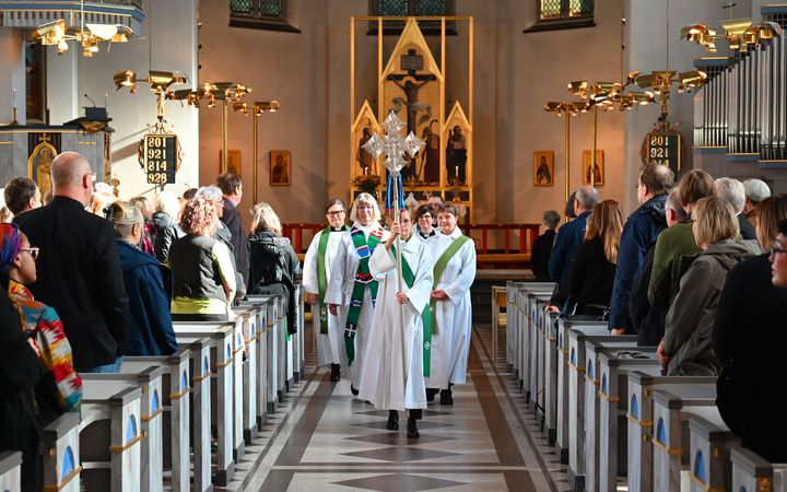 En procession av präster och ministranter går genom mittgången i en kyrka fylld med människor.