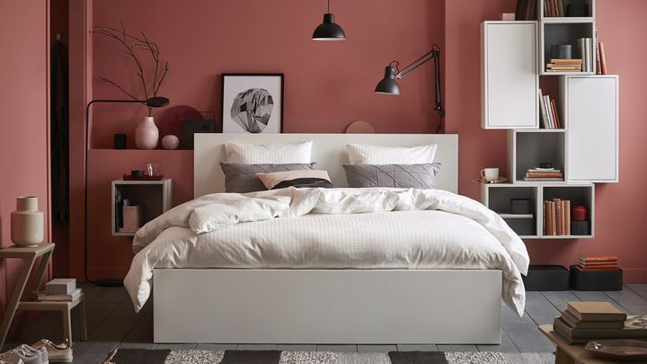 En vit säng står i ett sovrum med vinröda väggar.