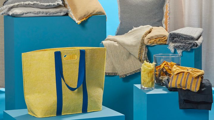 En tygpåse och flera filtar står tillsammans med IKEA:s personalkläder på blåa boxar.