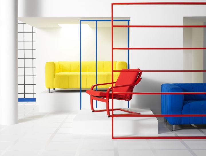 I ett ljust rum med vita väggar står en röd fåtölj och en gul och en blå soffa.