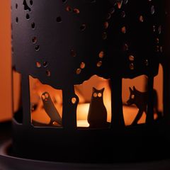 närbild på tänd, svart ljuslykta i metall med utstansade hål i form av djur och väsen som syns mot orange bakgrund