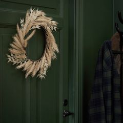 mörkgrön vägg och dörr med konstgjord krans i ljus halm som hänger på dörren