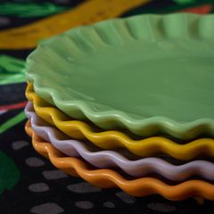 pastellfärgade assietter i färgerna orange, lila, gul, grön står på ett bord, staplade på varandra