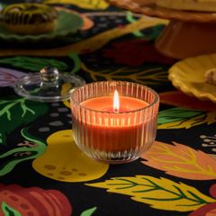 doftljus i klarglas och orangefärgat stearin står tänt på en pastellfärgad duk