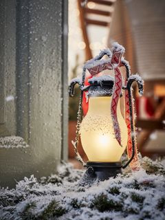 En upplyst lykta täckt av snö med ett rött och vitt band.