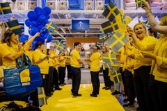 Grupp av människor i gula tröjor viftar med svenska flaggor inomhus.