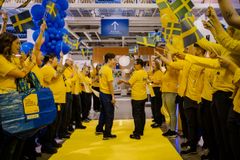 IKEA-medarbetare i gula tröjor håller svenska flaggor och blå ballonger redo att inviga.