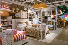 IKEA varuhus med bäddad säng, täcken och kuddar i en utställning. Lampor hänger i taket och hyllor med textilier syns i bakgrunden.