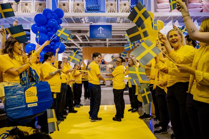 IKEA-medarbetare i gula tröjor håller svenska flaggor och blå ballonger redo att inviga.
