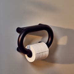 Toalettpappershållare av grafitgrå metall med en pappersrulle monterad.