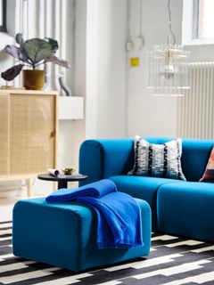 Modern vardagsrum med blå soffa och matchande ottoman. En svart-vit mönstrad matta täcker golvet.