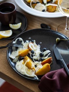 En svart tallrik med skivad gulbeta, blåbär, hackad lök och en krämig sås. Bredvid står ett glas vitt vin och en citronklyfta.