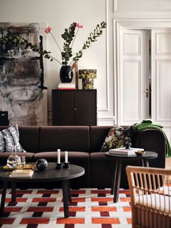 Vardagsrum med mörk soffa, två runda soffbord, blommor i vas och mönstrad matta i rött och vitt.