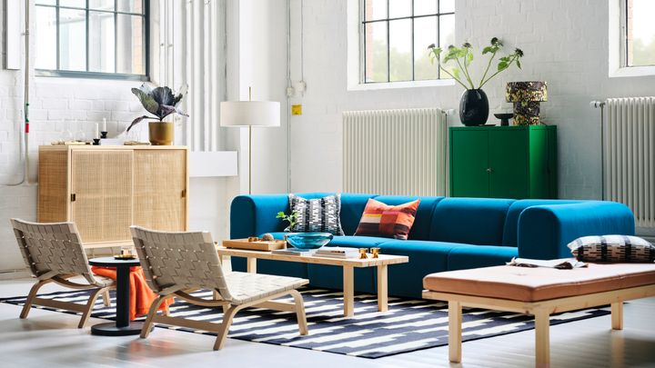 Ett%20ljust%20vardagsrum%20med%20en%20bl%E5%20soffa%2C%20tv%E5%20korgstolar%2C%20ett%20sk%E5p%20med%20skjutd%F6rrar%20i%20rotting%20och%20ett%20l%E5gt%20tr%E4bord%20i%20furu.%20P%E5%20golvet%20ligger%20en%20randig%20matta.