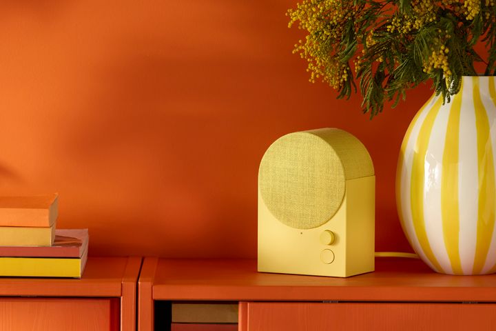 Gul%20h%F6gtalare%20och%20vit-gulrandig%20vas%20mot%20en%20orange%20bakgrund.