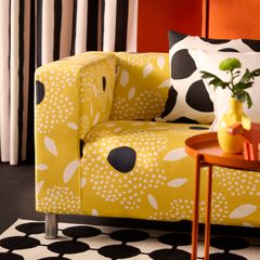 Gul soffa med svartvita blomliknande mönster, ett svartvitt randigt draperi i bakgrunden och ett svartvitt kuddfodral.