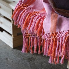 En rosa och orange pläd med fransar ligger över en trälåda.