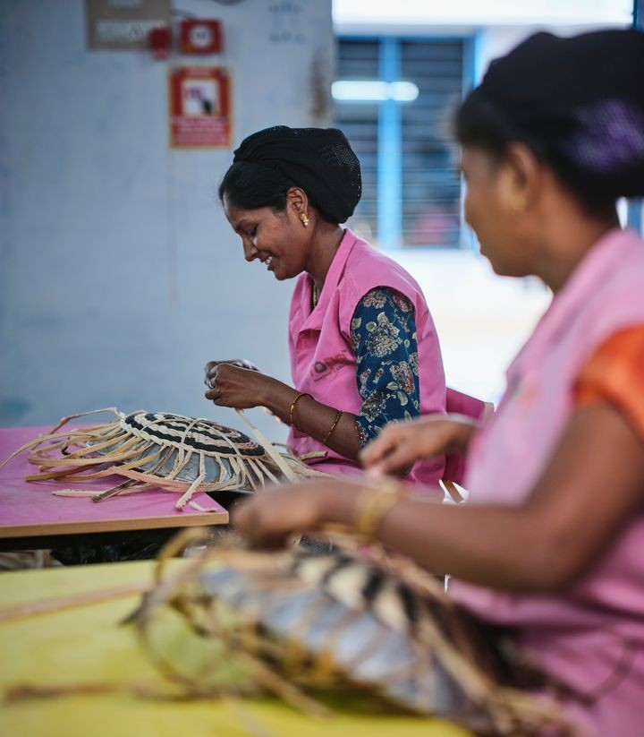 Tv%E5%20kvinnor%20i%20rosa%20f%F6rkl%E4den%20som%20v%E4ver%20korgar%20vid%20ett%20bord.