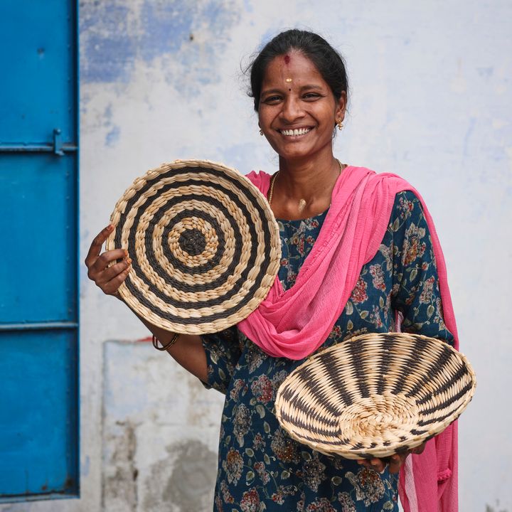 Leende person i färgglad klädsel håller två flätade korgar.