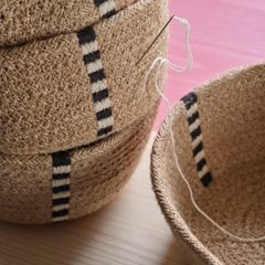 Flätade korgar i beige med svartvita ränder, en nål med tråd synlig.