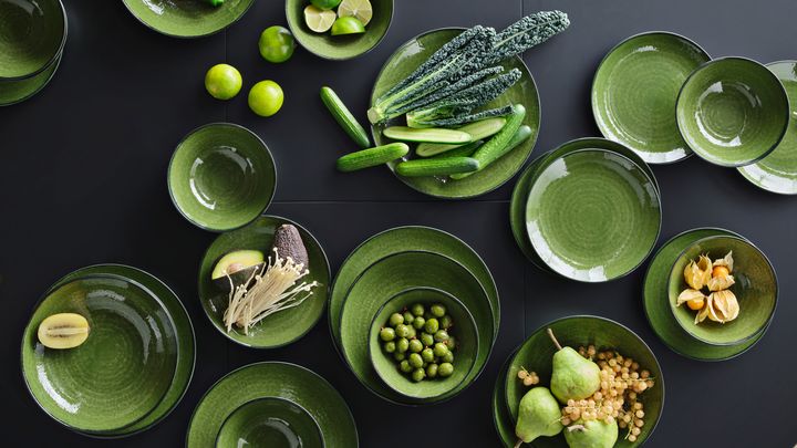 Gr%F6na%20sk%E5lar%20fyllda%20med%20olika%20frukter%20och%20gr%F6nsaker%2C%20inklusive%20p%E4ron%20och%20lime%2C%20p%E5%20ett%20svart%20bord.