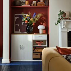 Vardagsrum med en vit hylla fylld med böcker, en blommig vas, och en bordslampa.