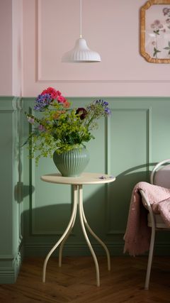 En krukväxt med färgglada blommor på ett litet runt bord i ett rum med gröna panelväggar.