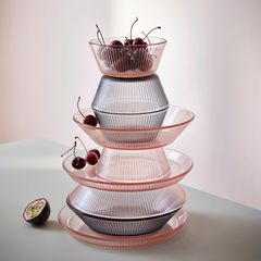 En stapel av olika storlekar av räfflade glasfat och skålar med körsbär på toppen, samt en uppskuren passionsfrukt bredvid.