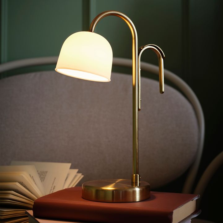 Bordslampa%20i%20m%E4ssing%20med%20vit%20sk%E4rm%2C%20lysande%2C%20st%E5r%20p%E5%20en%20trave%20b%F6cker.