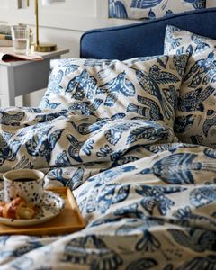 En säng med blåvitt mönstrat bäddset och en frukostbricka med kaffe och croissant på sängkanten.