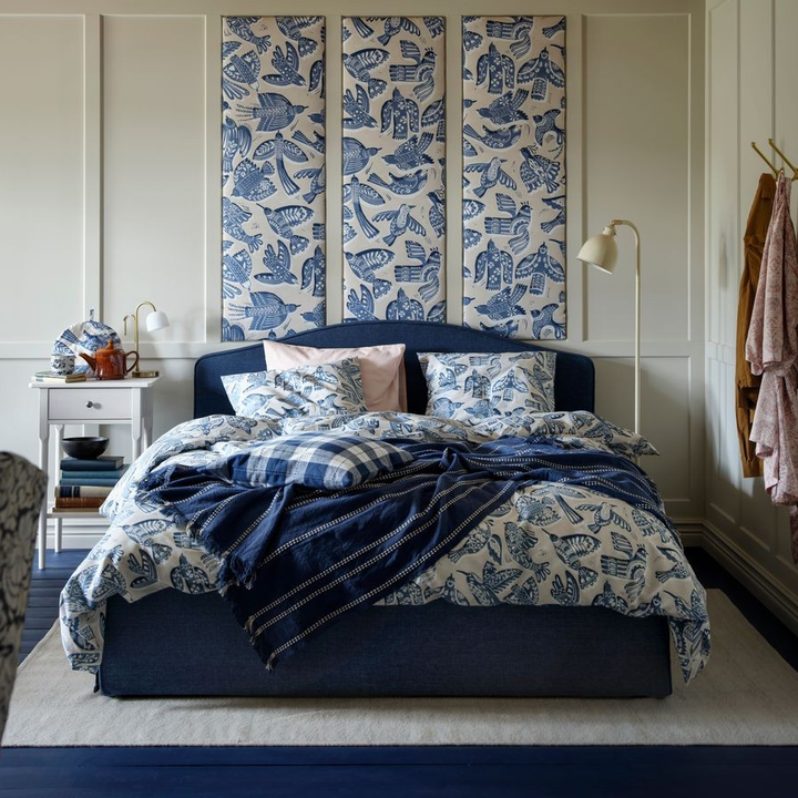 Ett%20sovrum%20med%20en%20s%E4ng%20kl%E4dd%20i%20bl%E5%20och%20vita%20s%E4ngkl%E4der%20med%20fiskmotiv.%20Tv%E5%20golvlampor%20st%E5r%20bredvid%20och%20kl%E4dh%E4ngare%20med%20morgonrockar%20syns%20till%20h%F6ger.%20En%20inredningstavla%20i%20bl%E5tt%20h%E4nger%20ovanf%F6r%20s%E4ngen.