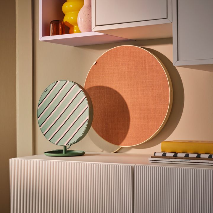 P%E5%20en%20b%E4nk%20st%E5r%20en%20rund%20h%F6gtalare%20i%20gr%F6nt%2C%20rosa%20och%20svart%20och%20p%E5%20v%E4ggen%20h%E4nger%20en%20st%F6rre%20rund%20h%F6gtalare%20som%20%E4r%20orange.