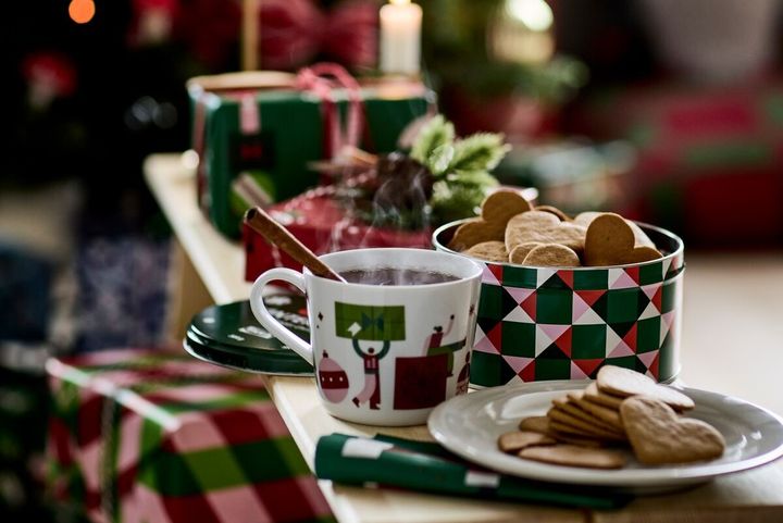 Ett%20bord%20med%20en%20julkopp%20med%20varm%20dryck%2C%20pepparkakor%20och%20juldekorationer%20i%20bakgrunden.