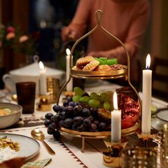 Ett dukat bord med tända ljus, en tvåvånings serveringsställning med frukt och kakor.
