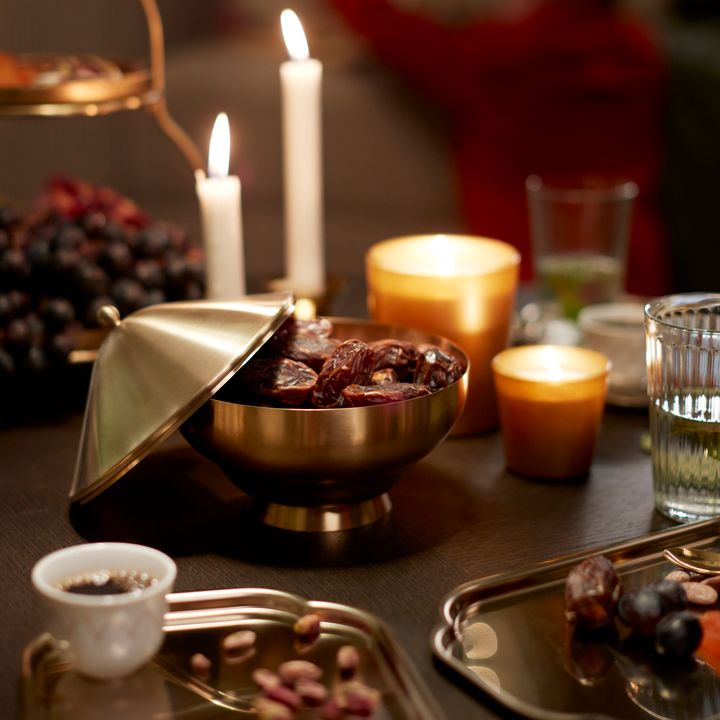 En%20elegant%20dukning%20med%20t%E4nda%20ljus%2C%20en%20sk%E5l%20med%20dadlar%20och%20olika%20sm%E5%20tilltugg%20p%E5%20ett%20bord.