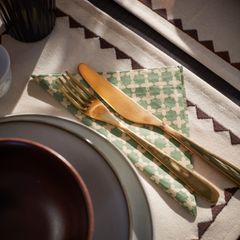 Matsalsdukning med guldbestick och en mönstrad servett på en duk.