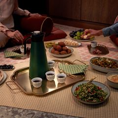 En matta med flera olika rätter, en termos, och små koppar placerade på en bricka för en måltid.