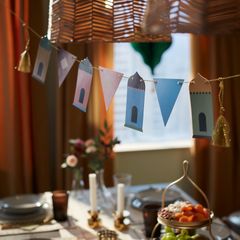 Pappersdekorationer i ljusa färger hänger på en linje över ett dukat bord.
