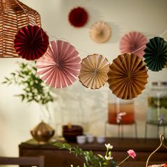 Dekorerade pappersrosetter upphängda på en rad i ett rum med växter och dryckesbehållare i bakgrunden.