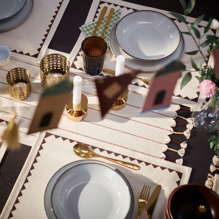 Dukning%20med%20tallrikar%2C%20bestick%20av%20guld%2C%20och%20t%E4nda%20ljus%20p%E5%20ett%20dekorativt%20bord.