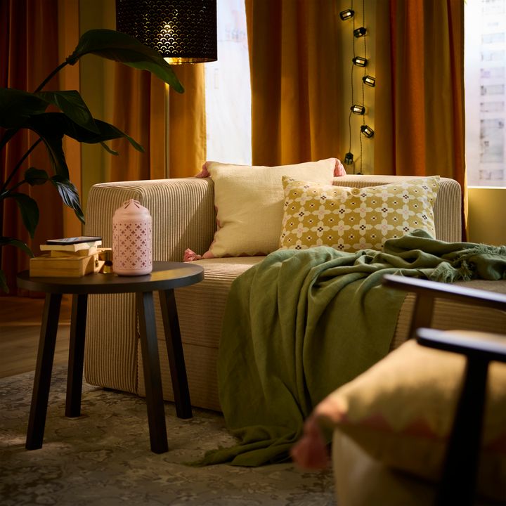 Alt%20text%3A%20Mysigt%20vardagsrum%20med%20soffa%2C%20kuddar%2C%20pl%E4d%20och%20sidobord%20med%20b%F6cker%20och%20en%20ljuslykta.