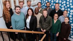 Tretton personer står i en trappa. Väggen är blå- och vitprickig.